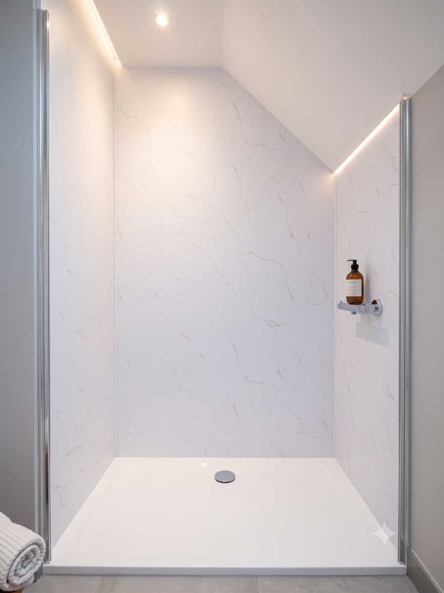 Douche effet marbre sous pente Douche moderne avec murs marbrés et étagère pour produits de bain.